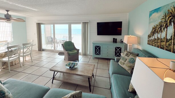 A living room with a sofa, a coffee table, a TV, and a painting of palm trees.
