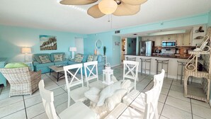 A living room with a blue sofa, white chairs, a dining table, and a ceiling fan.