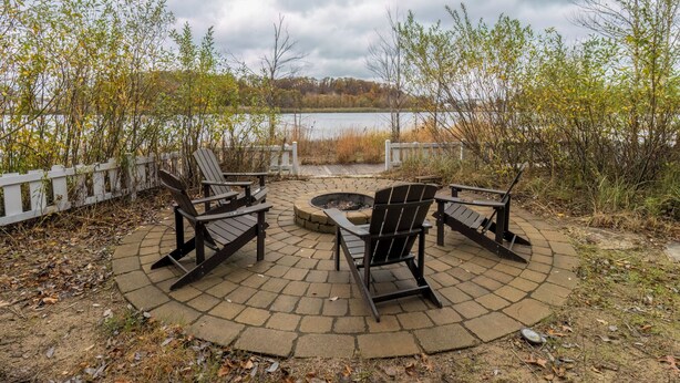 Un área de estar al aire libre con sillas Adirondack y un brasero, con vista a un lago.