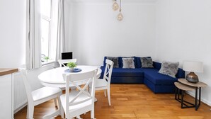 Una sala de estar moderna con una mesa de comedor blanca, sillas blancas, un sofá azul y una pequeña mesita de noche con una lámpara.
