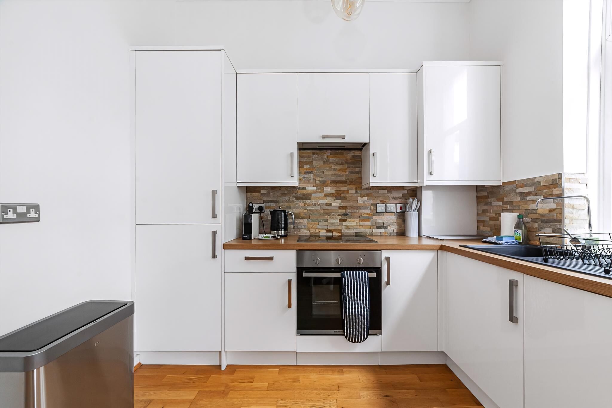 A modern kitchen with white cabinets, a wooden countertop, a built-in oven, and a stone backsplash.