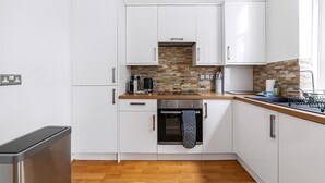 Una cocina moderna con armarios blancos, encimera de madera, horno empotrado y salpicadero de piedra.