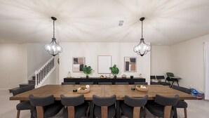 A spacious dining area with a long wooden table, six chairs, and two pendant lights. - Luxury 10 Bed w/Pool, Home Theater, & Gameroom! (Davenport)