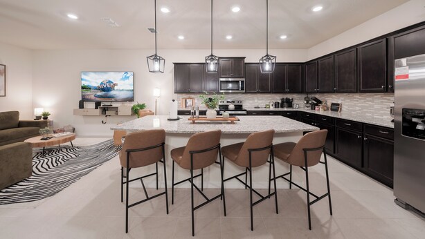 A modern kitchen with dark cabinets, a large island with bar stools, a flat-screen TV, and a refrigerator. - Luxury 10 Bed w/Pool, Home Theater, & Gameroom! (Davenport)