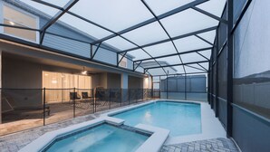 An indoor swimming pool with a glass ceiling, surrounded by lounge chairs and a covered patio area. - Luxury 10 Bed w/Pool, Home Theater, & Gameroom! (Davenport)