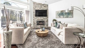 A modern living room with a stone fireplace, two sofas, a coffee table, and a large window.