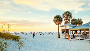 A beach scene with a covered pavilion, palm trees, and a sandy shore.