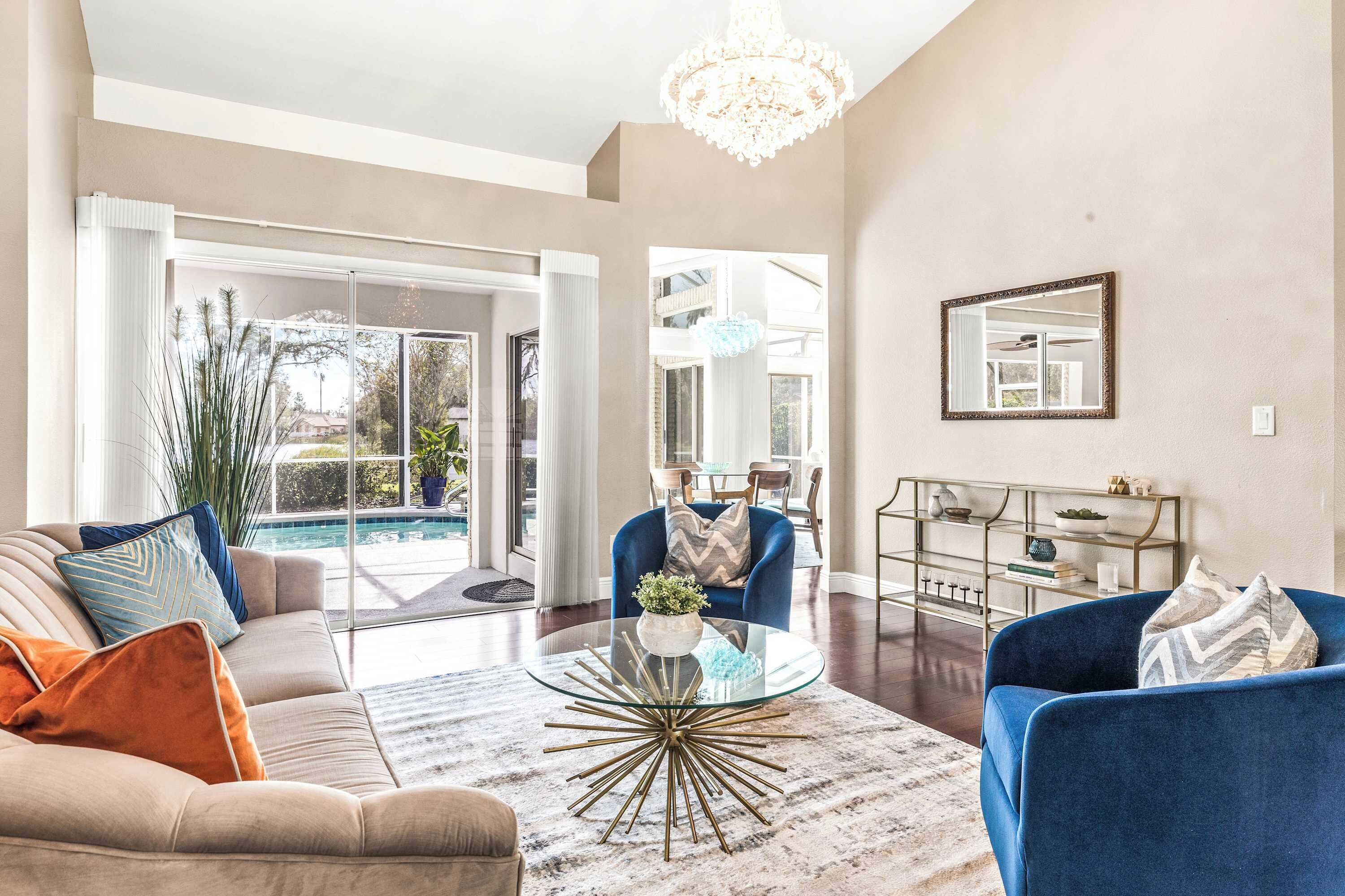 A modern living room with a glass coffee table, beige sofa, and blue armchair.