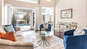 A modern living room with a glass coffee table, beige sofa, and blue armchair.