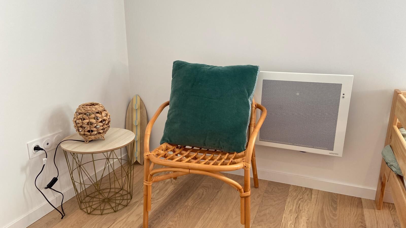 A wicker chair with a teal cushion, a round table with a woven stool, and a wall-mounted air conditioner.