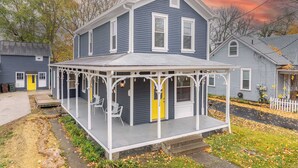 Une maison à deux étages avec un porche, une porte jaune et un toit gris.