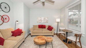 Un salon avec un canapé beige, des coussins rouges, une table basse en bois et un ventilateur de plafond.
