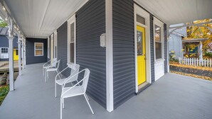 Un porche abrité avec des chaises en métal blanc et une porte jaune.