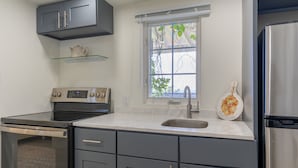 A kitchen with a stainless steel refrigerator, a built-in oven, a sink, and a window with a view of greenery. - Studio apartment above Horseshoe Bay beach (Southampton Parish)