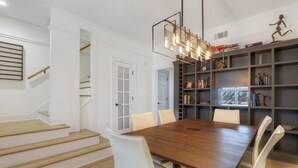 Un coin repas avec une table en bois et des chaises blanches, un escalier et une bibliothèque contenant divers objets.