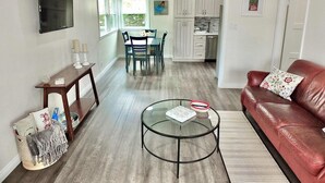 A modern living room with a glass coffee table, a red leather sofa, and a dining area with a table and chairs. - New Remodel, Minutes to Beach, Perfect for 2 (Long Beach)