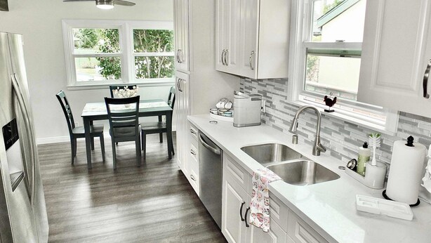 A modern kitchen with white cabinets, a double sink, and a dining area with a table and chairs. - New Remodel, Minutes to Beach, Perfect for 2 (Long Beach)