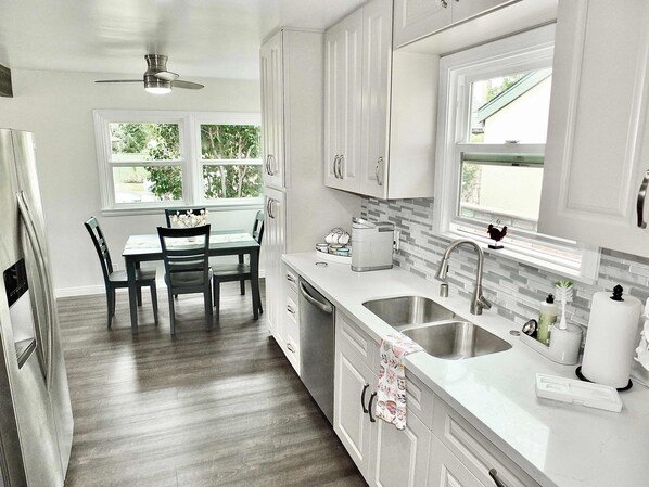 A kitchen with white cabinets, a dining table with chairs, a window, and a ceiling fan.