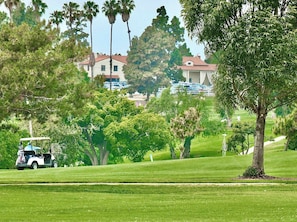 Um campo de golfe com um carrinho de golfe, árvores e um edifício ao fundo.