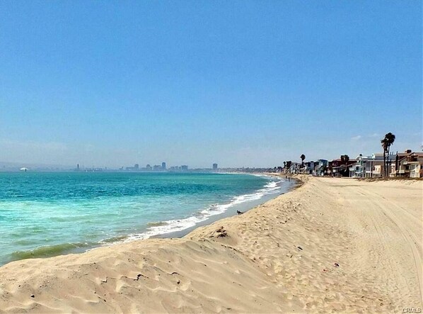 A beach with a clear view of the ocean, a sandy shore, and a row of buildings along the coastline.