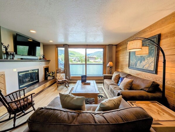 A spacious living room with a fireplace, a large sofa, a coffee table, and a television mounted on the wall. - Cozy Winter Escape | Pool + Hot Tub, Shuttle (Keystone)