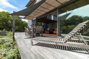 Une terrasse en bois agrémentée de mobilier d’extérieur, d’une pergola et d’un mur de verre qui reflète le paysage environnant.