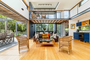 Un amplio salón con techo alto, un balcón con mobiliario de mimbre y una cocina con armarios azules.