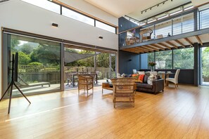 Un salón amplio con un gran ventanal que da a un patio exterior, un sofá, una mesa de centro y un comedor con sillas.