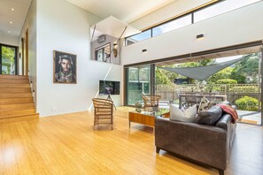 Amplia sala de estar con piso de madera, un sofá marrón y una mesa de comedor con sillas. Una ventana grande ofrece vistas al exterior.