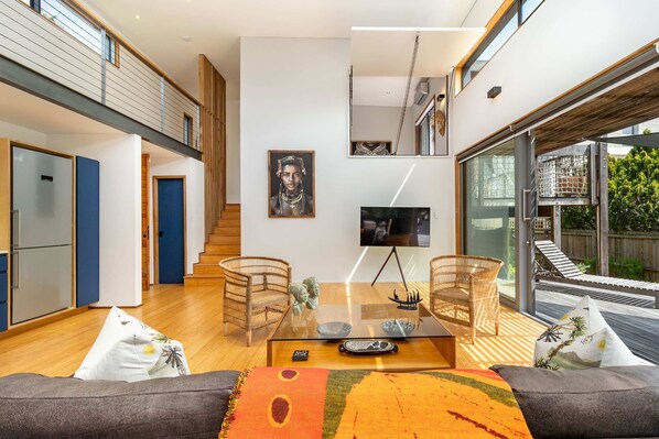 Una sala de estar moderna con una mesa de centro de vidrio, dos sillas de mimbre, un sofá y un gran ventanal con vistas a una terraza.
