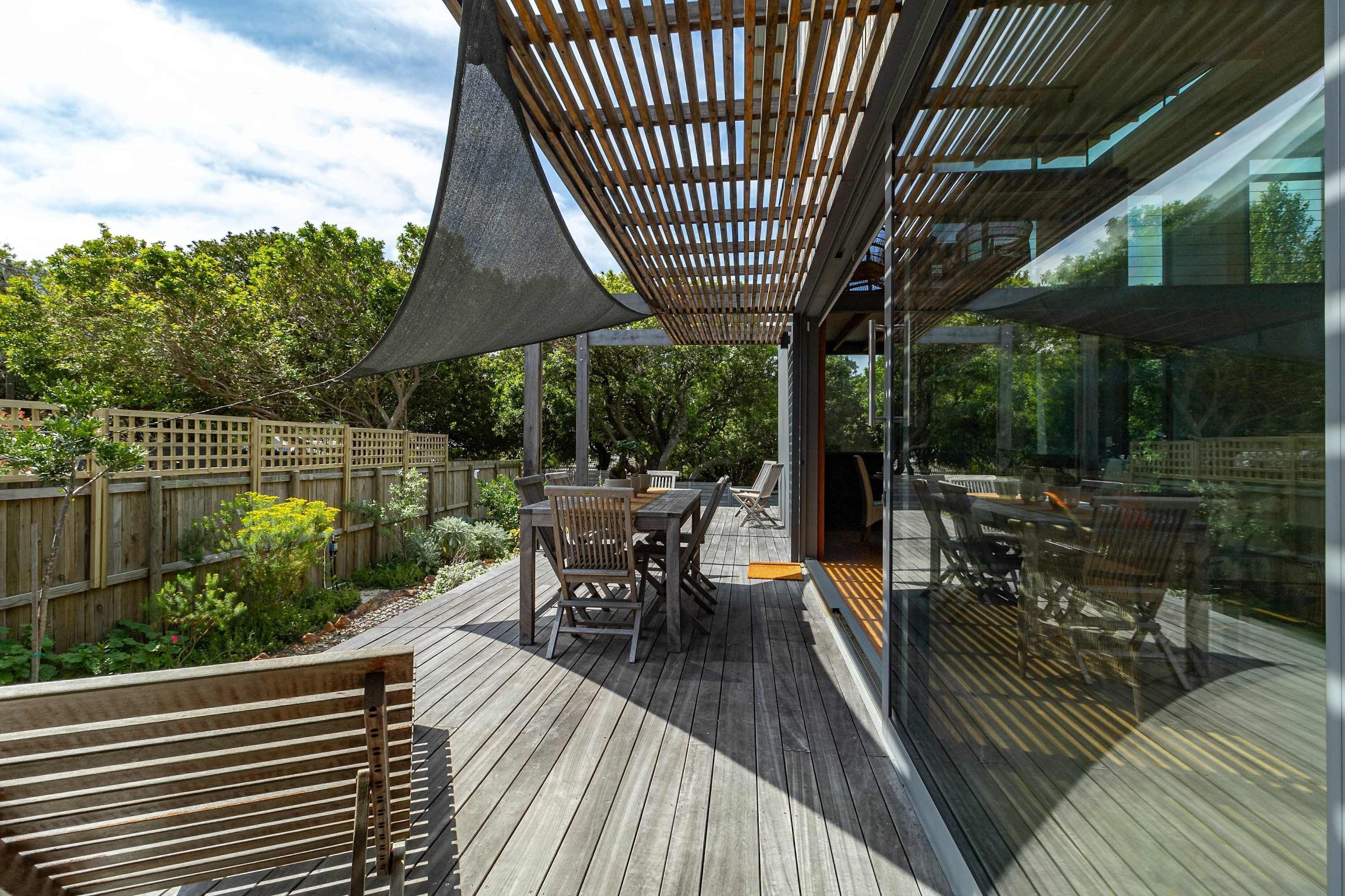 An outdoor deck with wooden furniture, a pergola, and a glass enclosure.