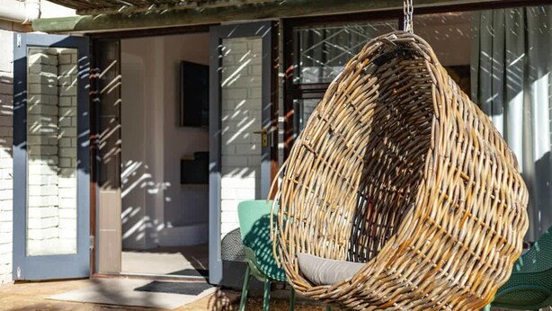 A wicker hanging chair with a cushion, green chairs, and a glass door entrance. - Charming Garden Cottage-campsbay (Cape Town)