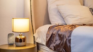A neatly made bed with white linens and a brown blanket, a bedside lamp with a gold base, and a small, textured object on the nightstand. - Charming Garden Cottage-campsbay (Cape Town)