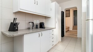 A modern kitchen with white cabinets, a granite countertop, and a coffee maker. - Charming Garden Cottage-campsbay (Cape Town)