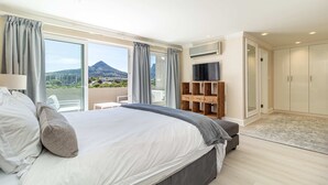 Une chambre avec un grand lit, une télévision et une armoire. La fenêtre offre une vue sur une montagne.