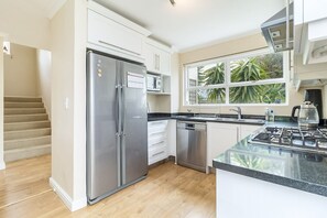 A modern kitchen with stainless steel appliances, a dishwasher, a stove, and a window with a view of greenery. - 3 Bedroom Family Home - Houtbay (Cape Town)