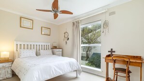 A bedroom with a bed, a desk, a chair, a ceiling fan, and a window with curtains. - 3 Bedroom Family Home - Houtbay (Cape Town)