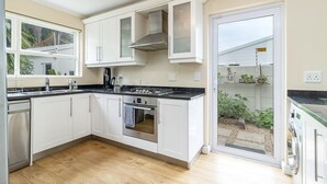 A modern kitchen with white cabinets, a stainless steel range hood, and a built-in oven. - 3 Bedroom Family Home - Houtbay (Cape Town)