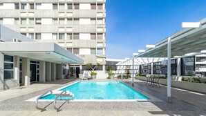 A swimming pool with a clear blue water, surrounded by a covered area with chairs and potted plants.