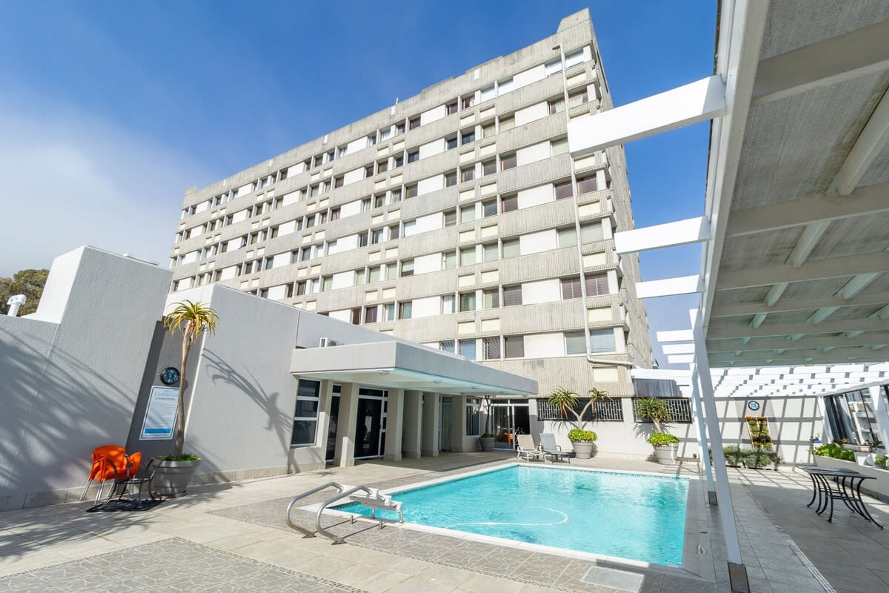 A hotel with a pool area, a covered seating area, and a large building in the background.