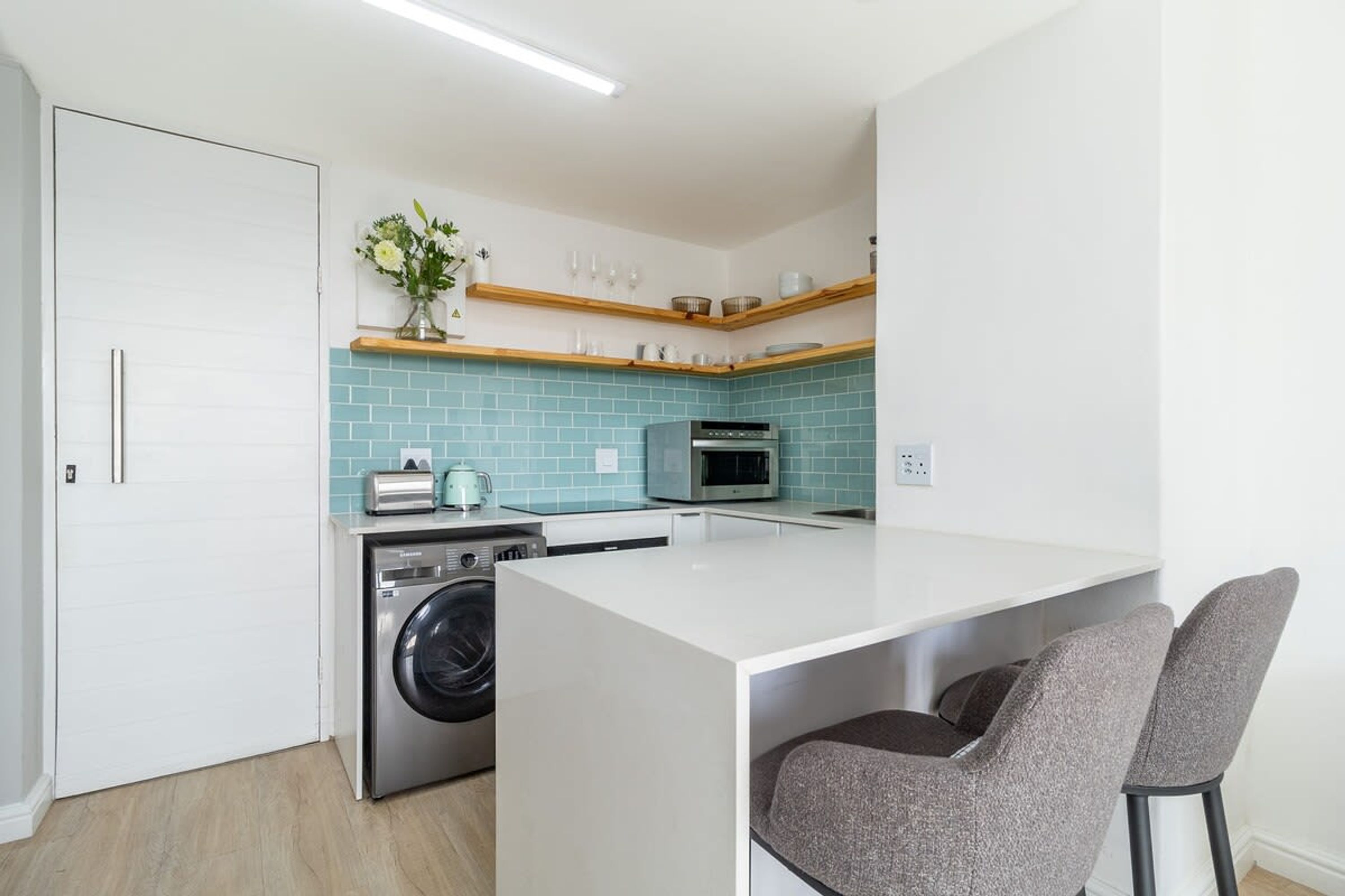 A compact kitchen with a washing machine, microwave, and a small island with chairs.