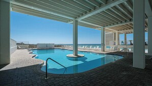 A covered outdoor swimming pool with a clear view of the ocean, surrounded by lounge chairs and a tiled deck.