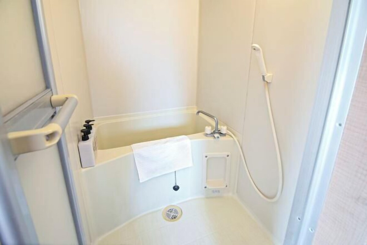 A small, white, walk-in shower with a handheld showerhead, a towel rack, and a control panel.