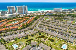 A residential area with multiple apartment buildings, a swimming pool, and a view of the ocean. - The Turtle Nest | Pool, Beach Access | Activity Experiences (Panama City Beach)