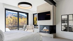 Een moderne slaapkamer met een groot bed, een open haard en een balkon met uitzicht op de bergen.