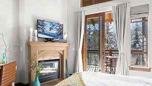 A cozy room with a fireplace, a bed, a TV, and a balcony with a view of snow-covered trees. - Serenity King | Balcony (Park City)