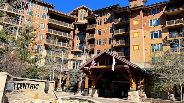 A multi-story hotel with a stone facade, balconies, and a central entrance with a wooden structure. - Serenity King | Balcony (Park City)