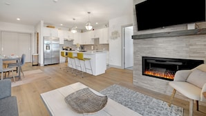Una cocina moderna con armarios blancos, una isla central con taburetes amarillos y una chimenea empotrada.
