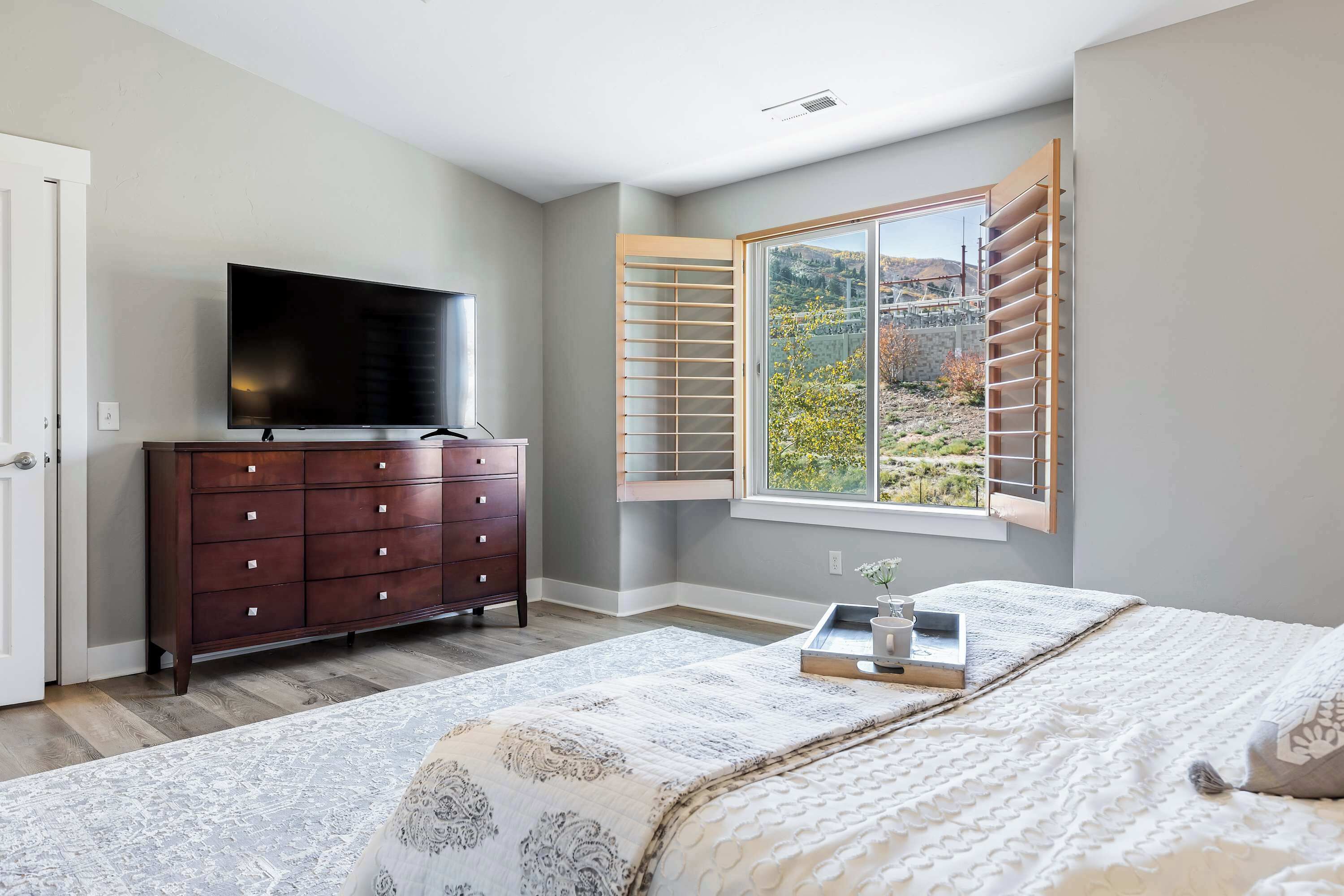 Un dormitorio con una cama grande, un aparador, un televisor y una ventana con contraventanas.