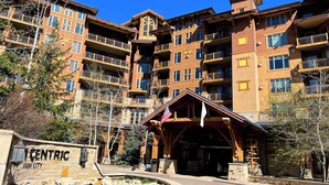 Un hotel de varios pisos con fachada de piedra, balcones y una entrada central con estructura de madera.